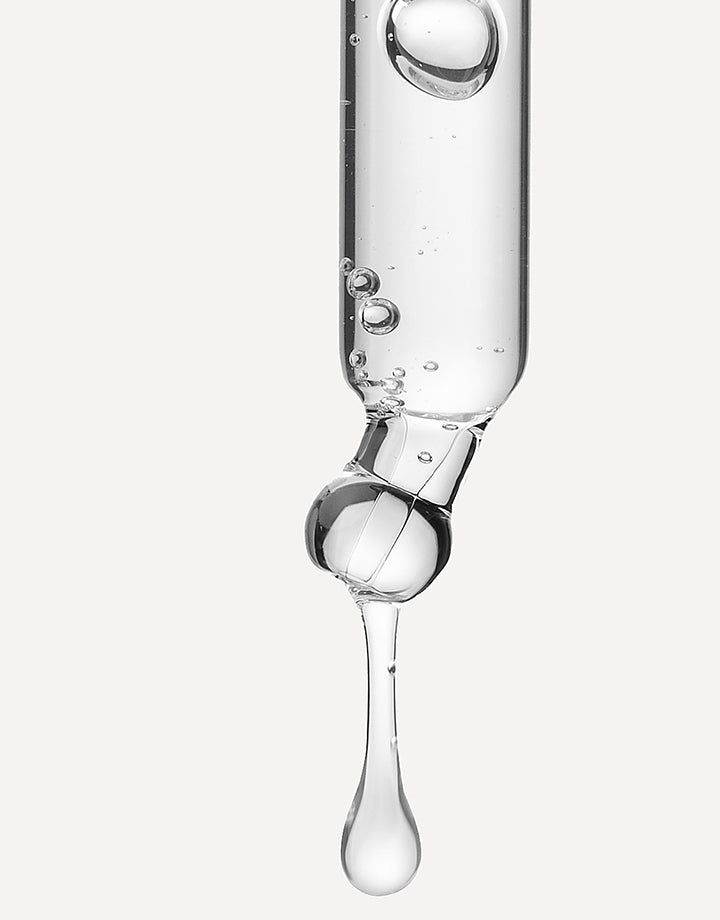 Pipeta con sérum transparente liberando una gota sobre fondo neutro.